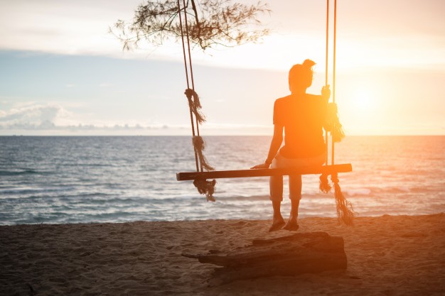 young-woman-watching-sunset-alone-sitting-on-swings-on-the-beach-at-sunset_1150-2174